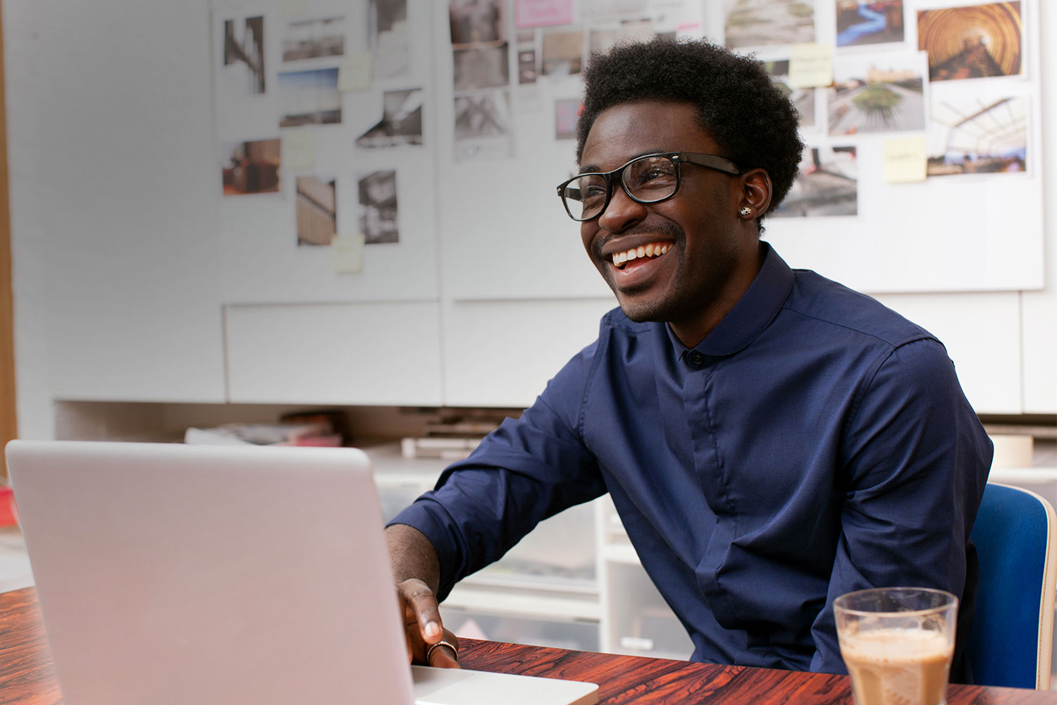 Man smiling while sitting at a desk in front of an open laptop